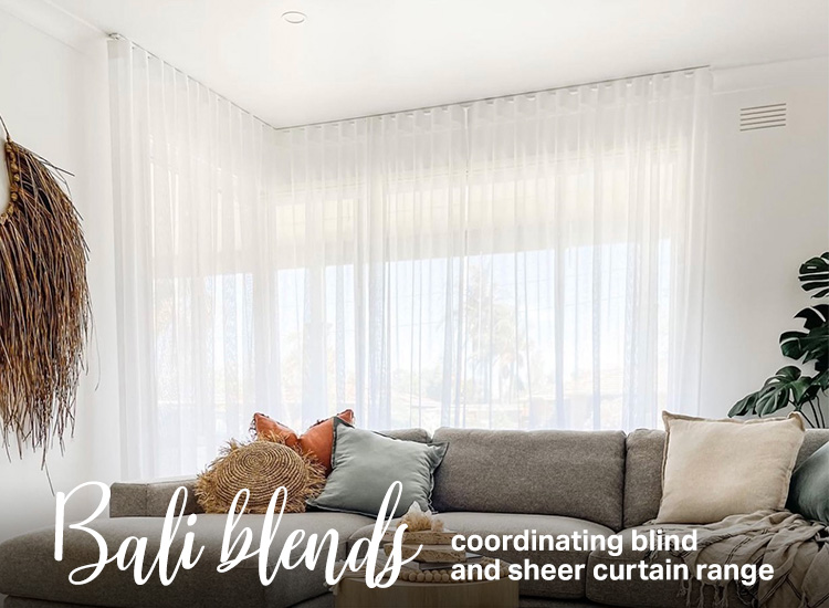 Beautifully styled living room with grey couch and white sheer curtains on the corner window. 