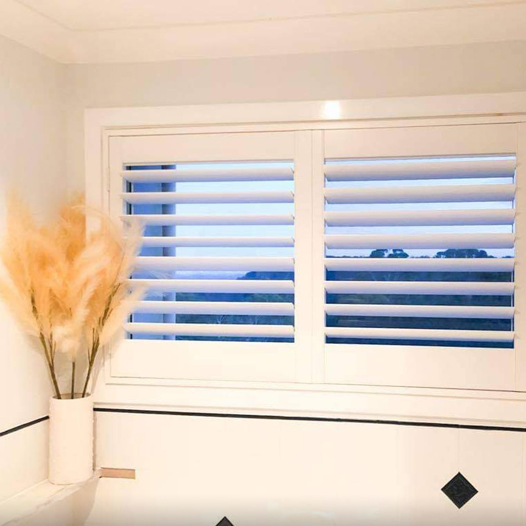 Modern white bathroom featuring a Plantation Shutter above a bath.