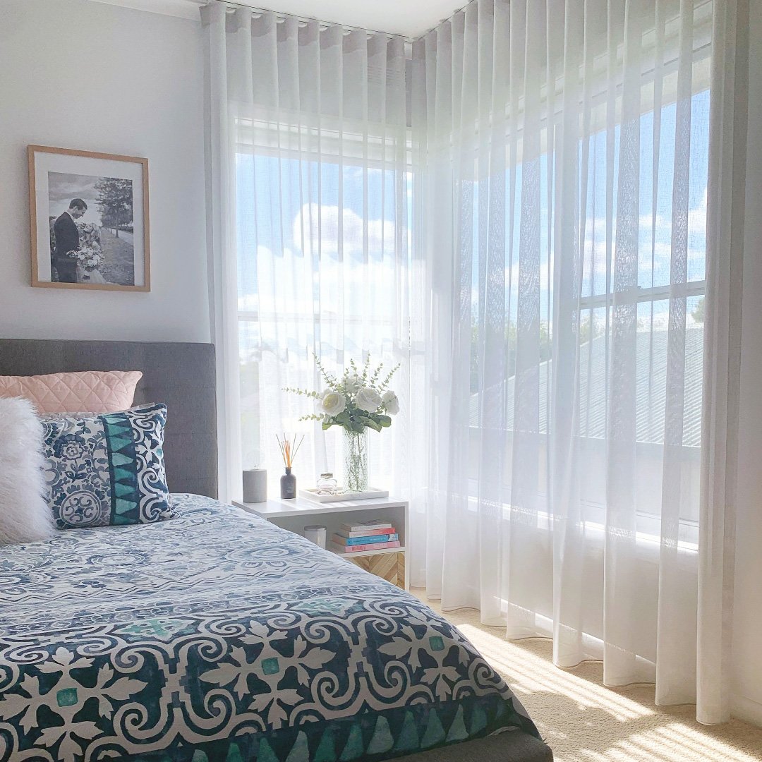 Light grey sheer curtains on a corner window in a bedroom. 