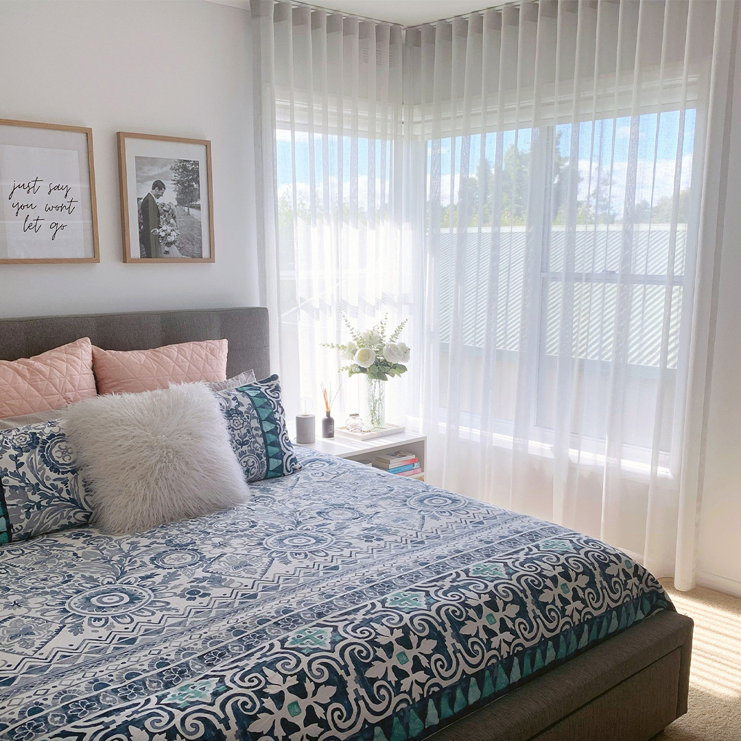 Light grey sheer curtains on a corner window in a bedroom. 